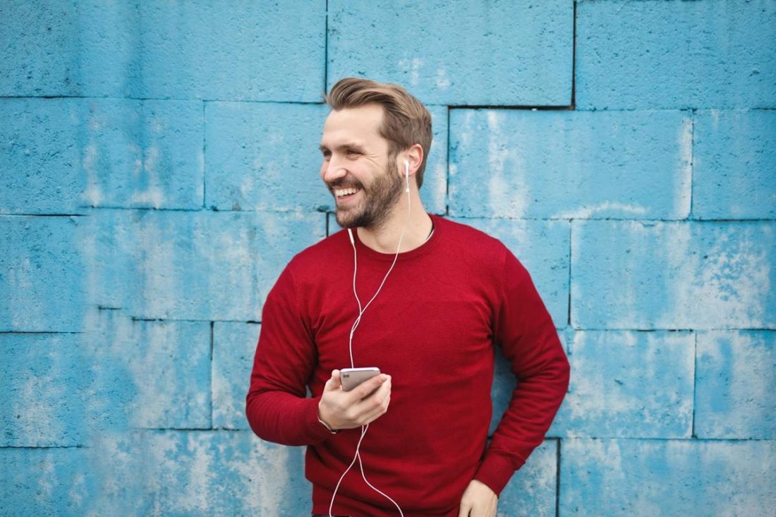 Un hombre usando su teléfono a una distancia segura y utilizando auriculares mientras atiende una llamada. (De: Pexels)