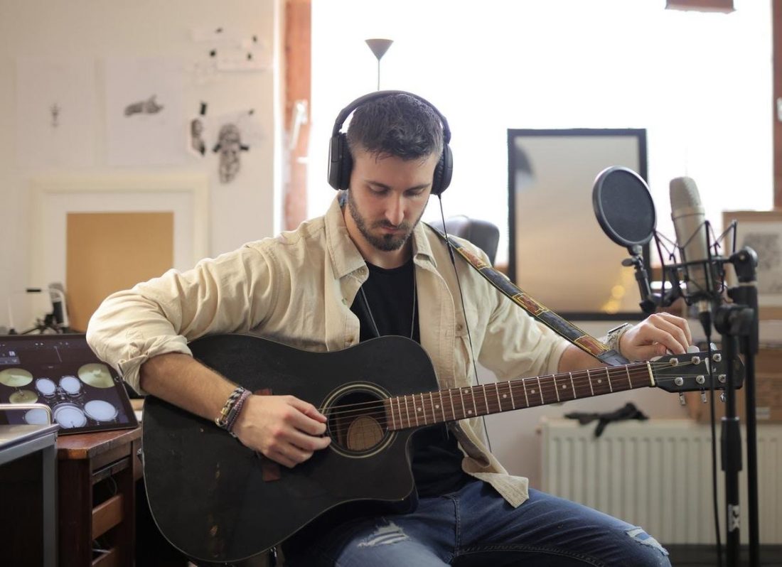 Un hombre toca la guitarra con los auriculares puestos (De Pexels.com)