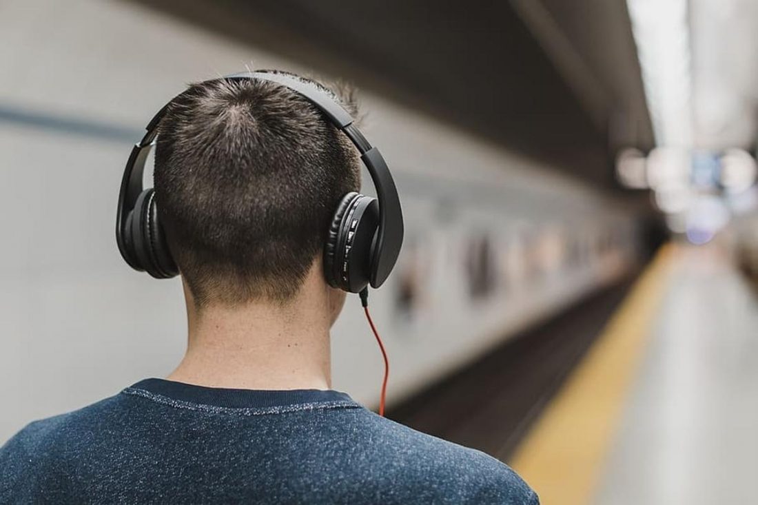 Hombre caminando en la estación de tren con los auriculares puestos (De: pxfuel.com)